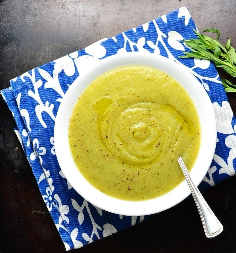 Top down view of easy zucchini soup in white bowl with spoon on blue cloth.
