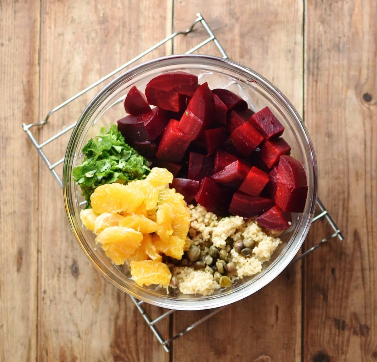 Top down view of cubed beetroot, orange pieces, herbs and cooked quinoa inside translucent bowl.