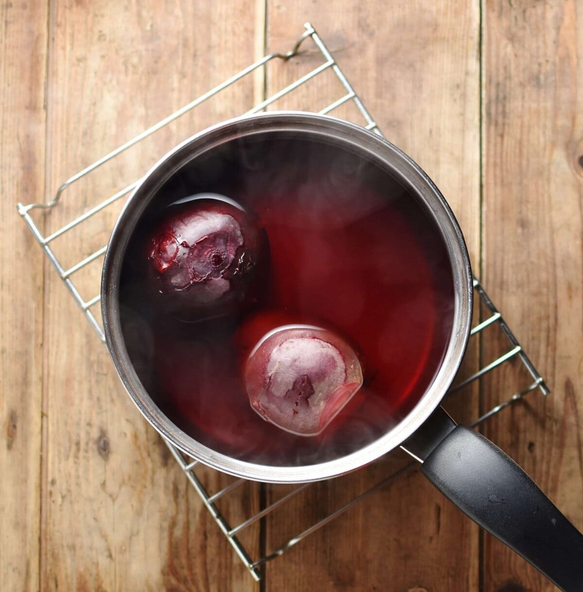 2 beets in water inside saucepan on top of cooling rack.