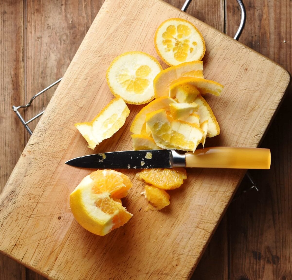 Peeled orange with knife on top of cutting board.