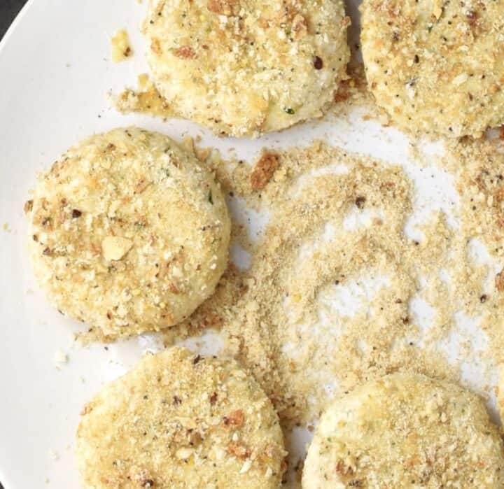 Coating cauliflower patties in breadcrumbs on plate.