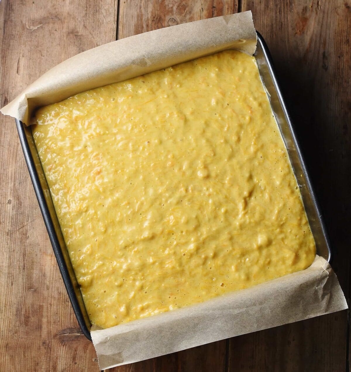 Unbaked pumpkin cake inside square pan with parchment paper sticking out.