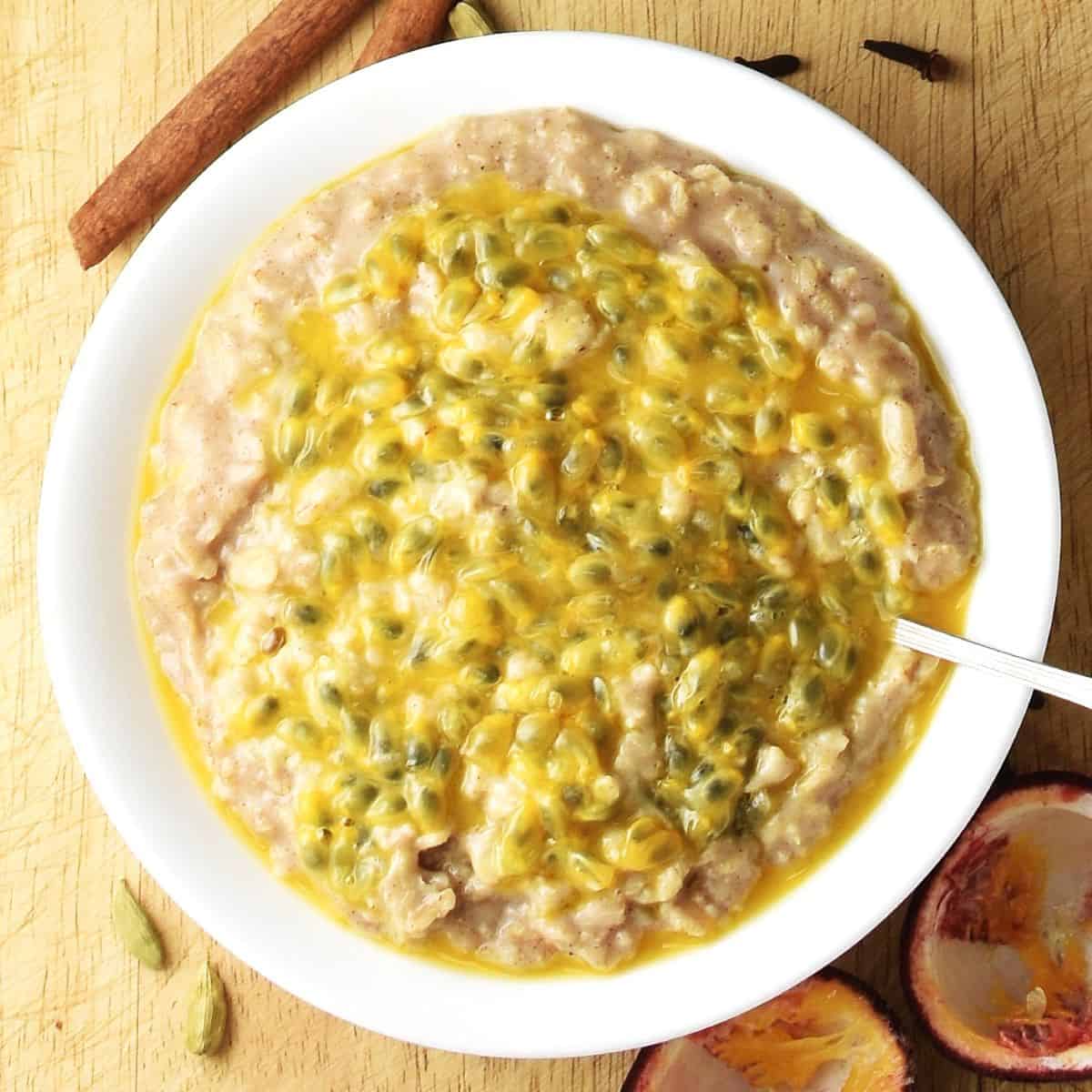 Top down view of chai oatmeal topped with passion fruit in white bowl with spoon. 