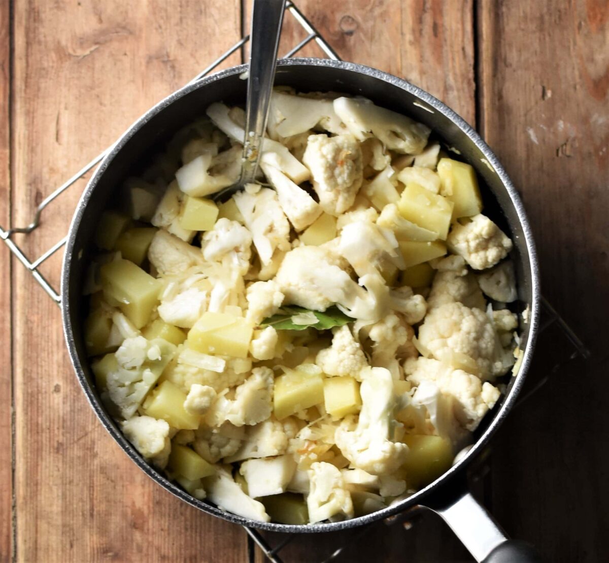 Cauliflower pieces and cubed potatoes in large pot with spoon.