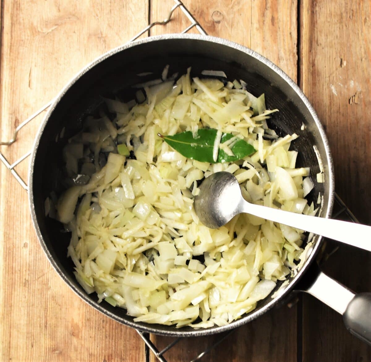 Chopped onion and bay leaf in large pot with spoon.