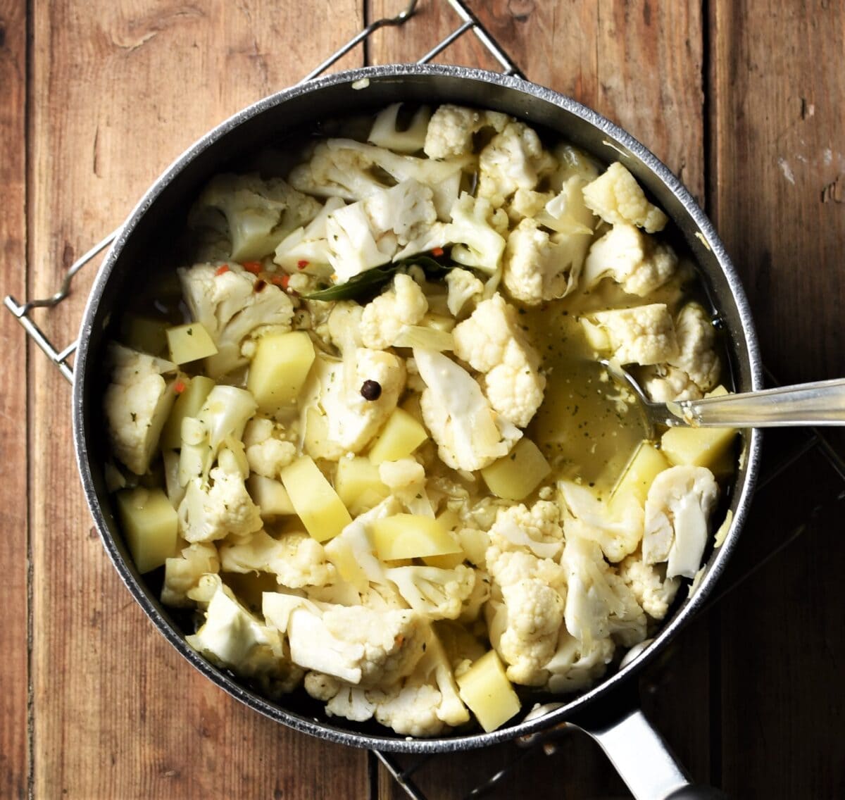 Cubed potato and chopped cauliflower in large pot with spoon.