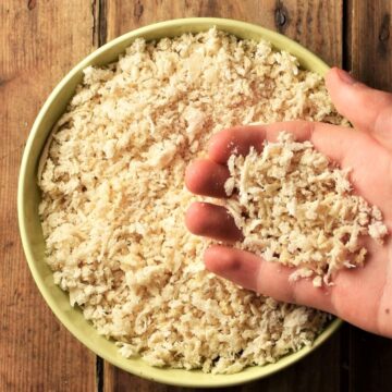 Hand holding homemade breadcrumbs over yellow bowl.