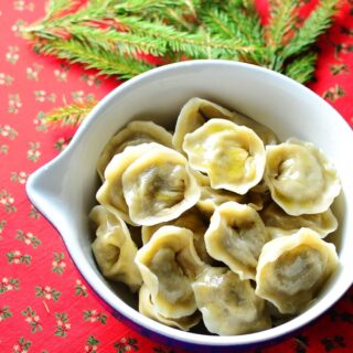 Polish Christmas Eve porcini dumplings (uszka) in white bowl with pine tree branch on red cloth with hollies pattern.