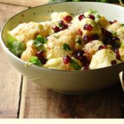 Side view of cauliflower salad in green bowl, with herbs in background.