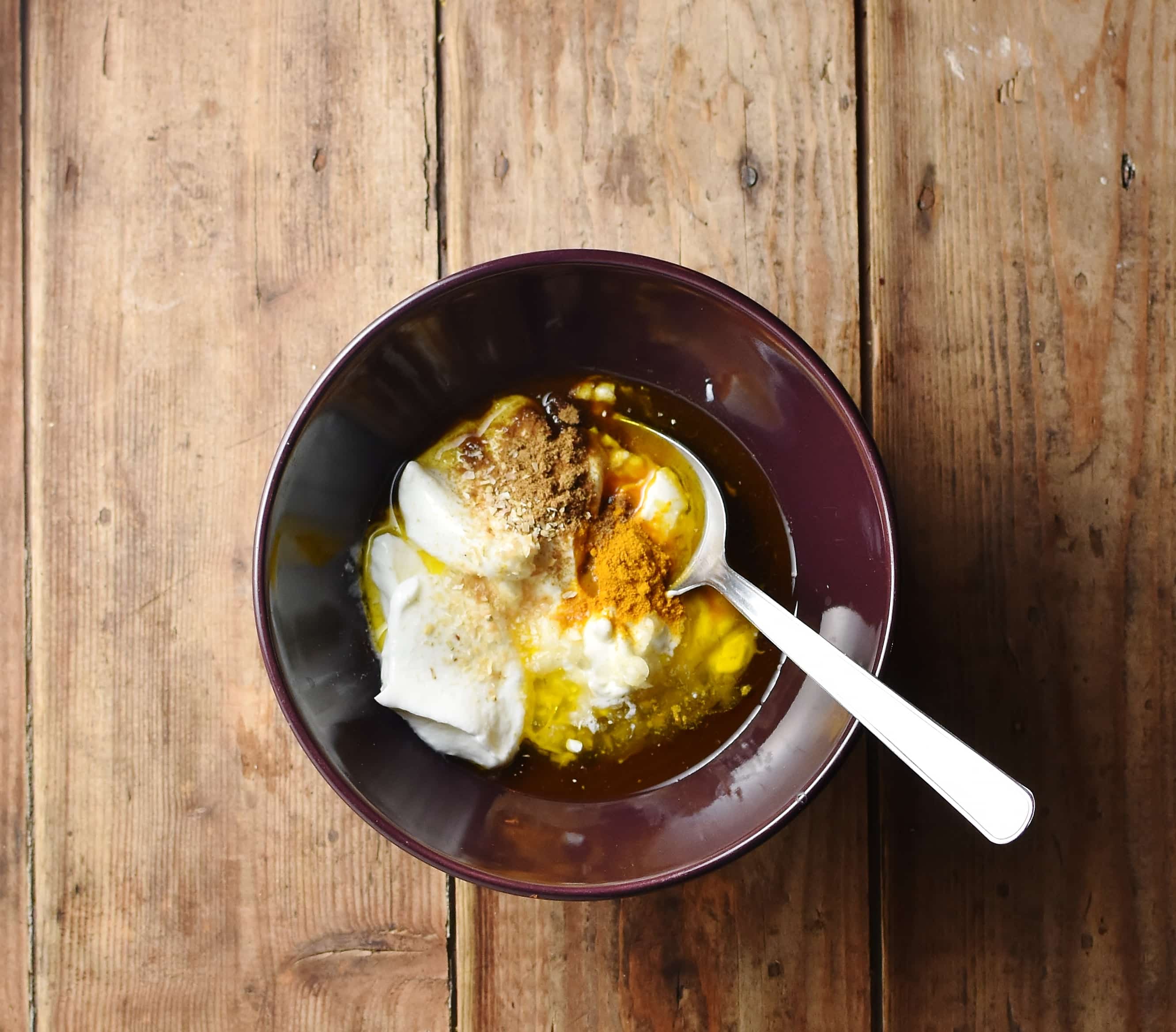 Yogurt, spices and oil in purple bowl with spoon.
