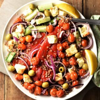 Top down view of roasted vegetables, feta and lemon wedges with buckwheat on large plate.