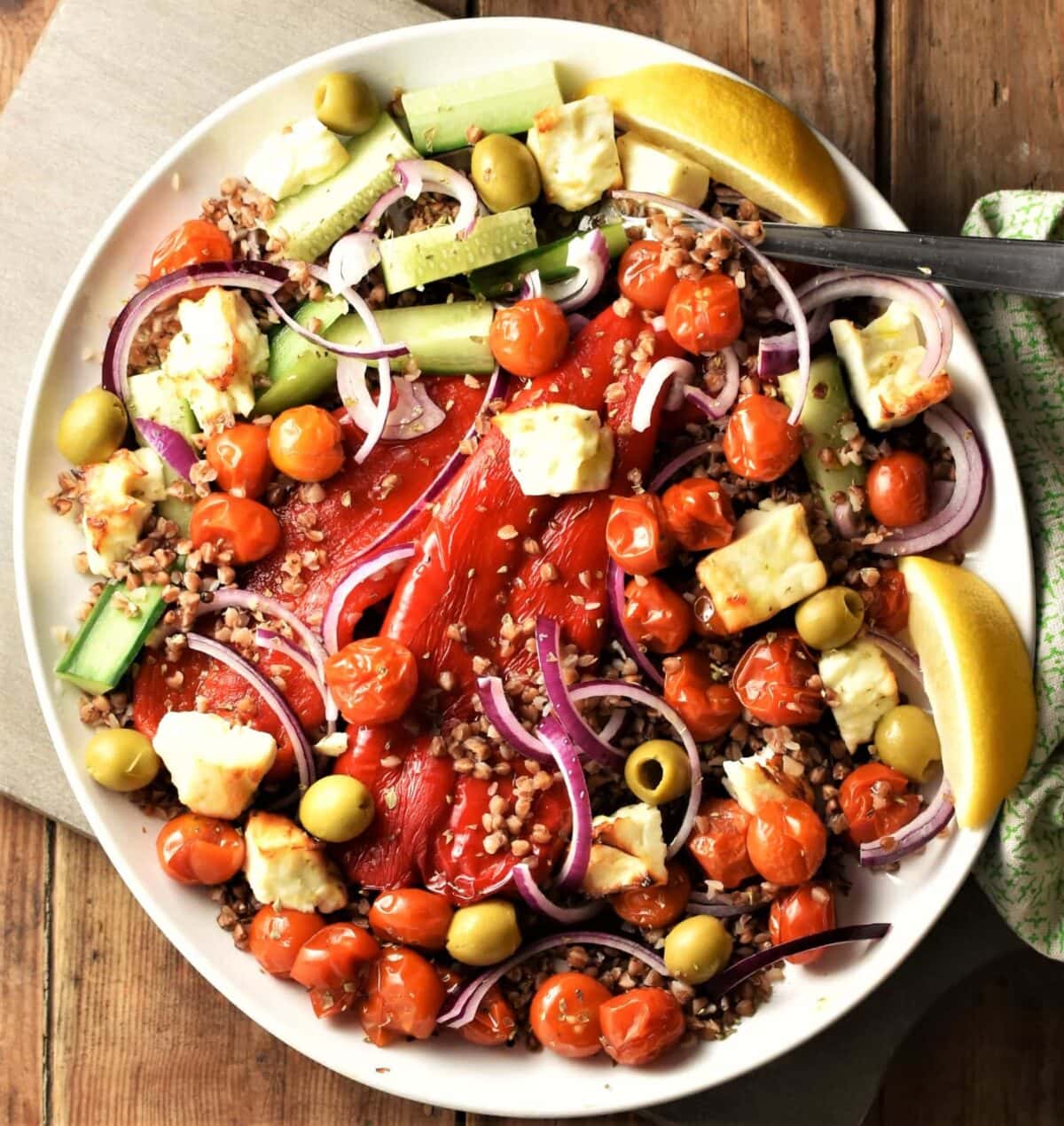 Top down view of roasted vegetables, feta and lemon wedges with buckwheat on large plate.