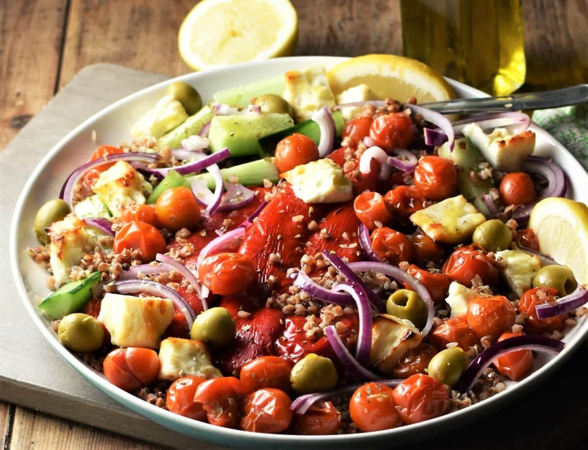 Side view of buckwheat salad with roasted vegetables, olives and feta on white plate.