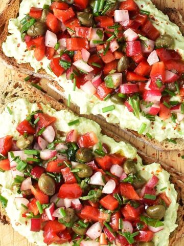 Top down view of 2 avocado ricotta toasts with chopped vegetables.