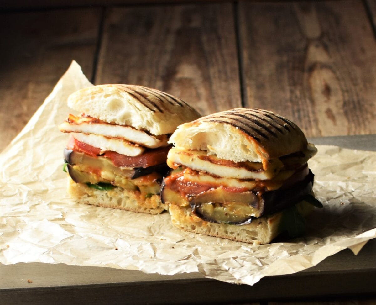 Side view of eggplant sandwich cut in half on top of paper.