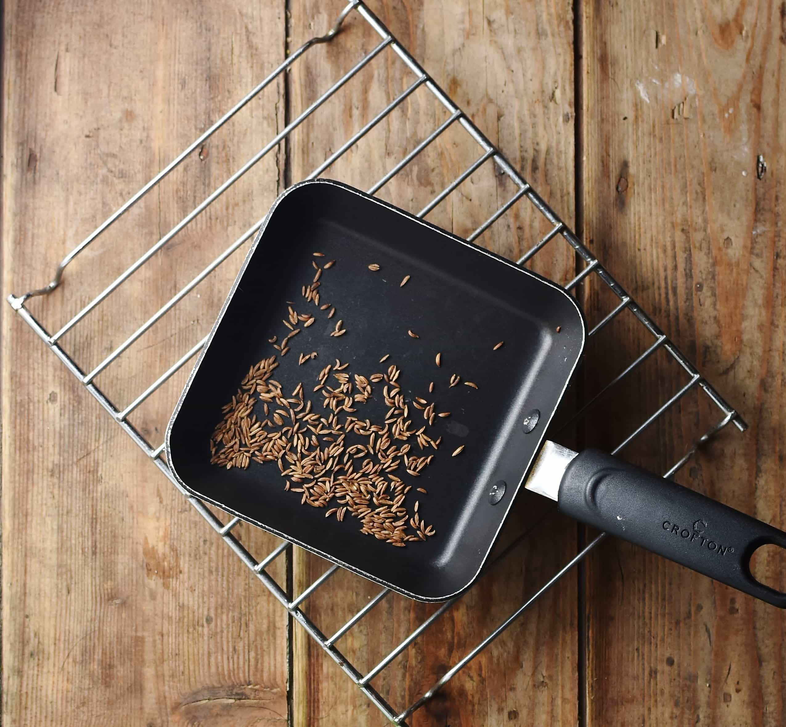 Caraway seeds in small square pan on top of rack.