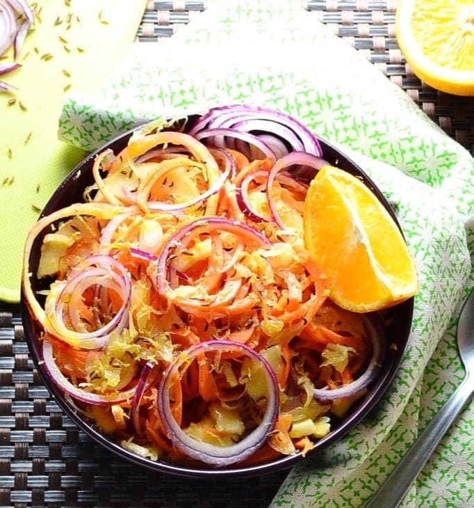 Top down view of sauerkraut carrot salad in purple bowl with orange, green cloth and partial view of yellow board.