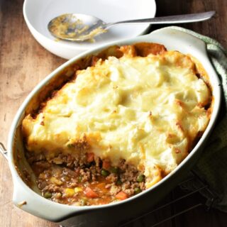 Side view of turkey cottage pie in oval green dish with white bowl and spoon in background.