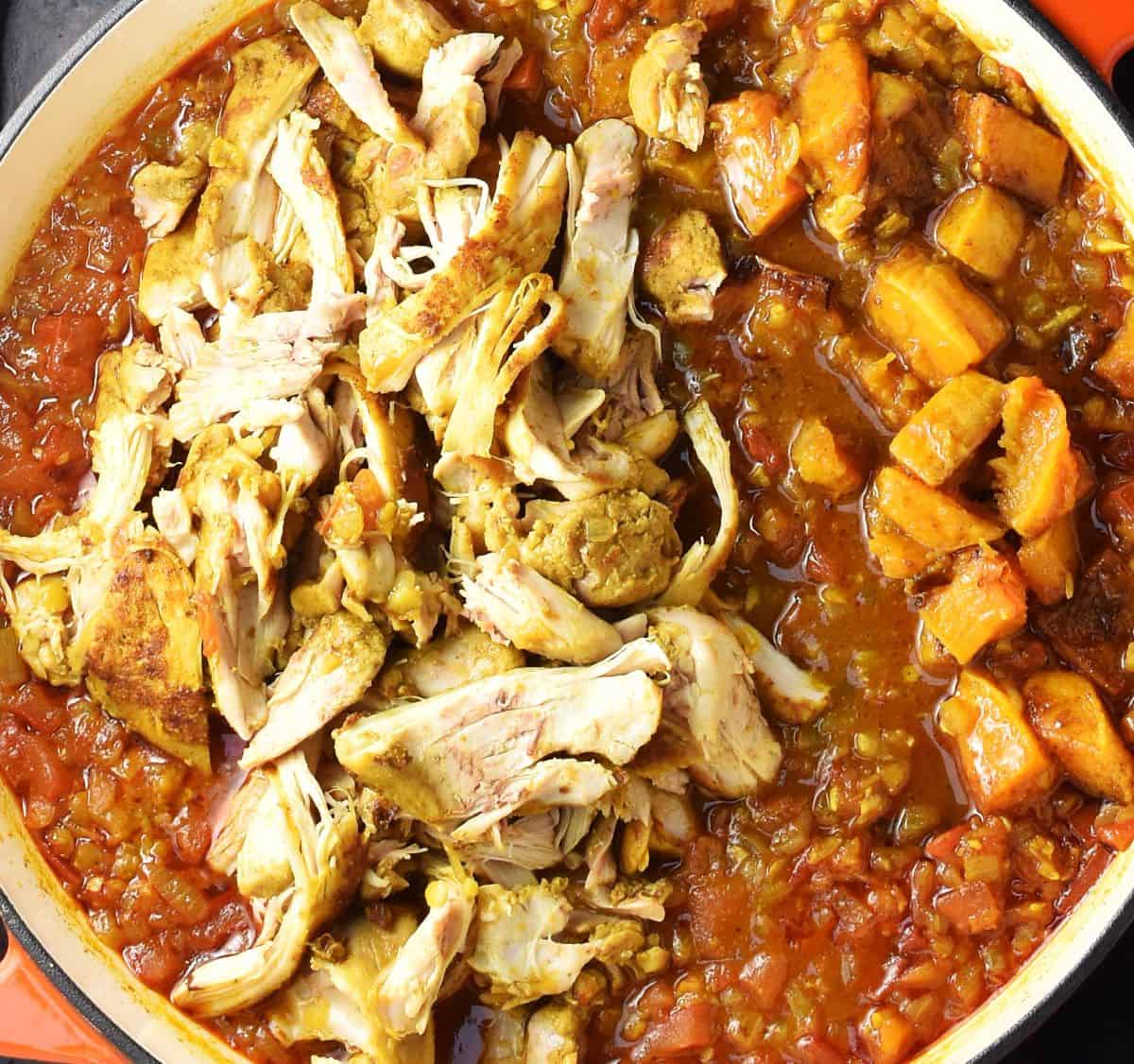 Top down view of chicken  and butternut squash pieces added to curry sauce in large pan.
