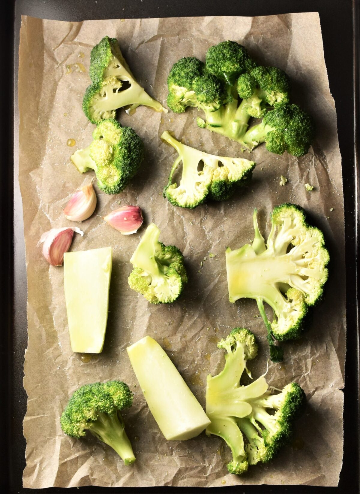 Sliced broccoli and 3 garlic cloves on top of parchment.
