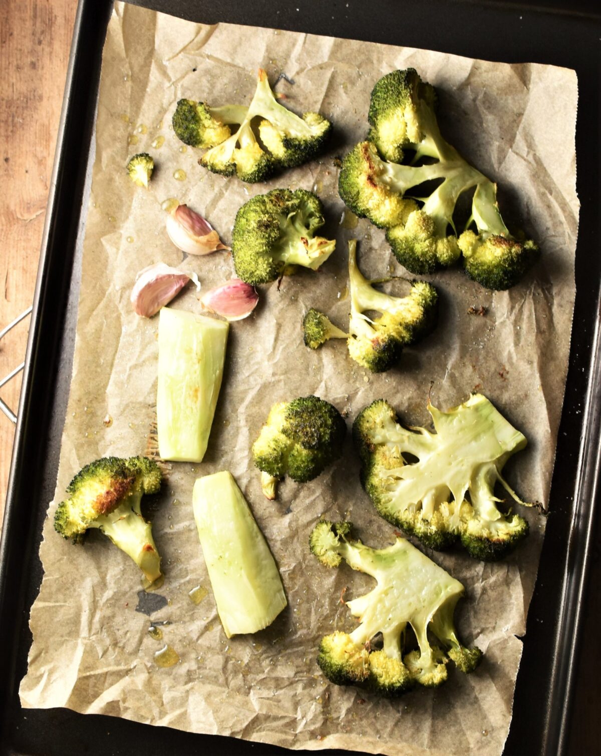 Roasted broccoli pieces and 3 garlic cloves on top of baking sheet lined with parchment.