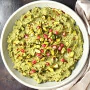 Top down view of broccoli hummus in grey bowl dressed with pistachios and pomegranate seeds.