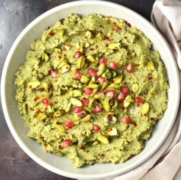 Top down view of broccoli hummus in grey bowl dressed with pistachios and pomegranate seeds.