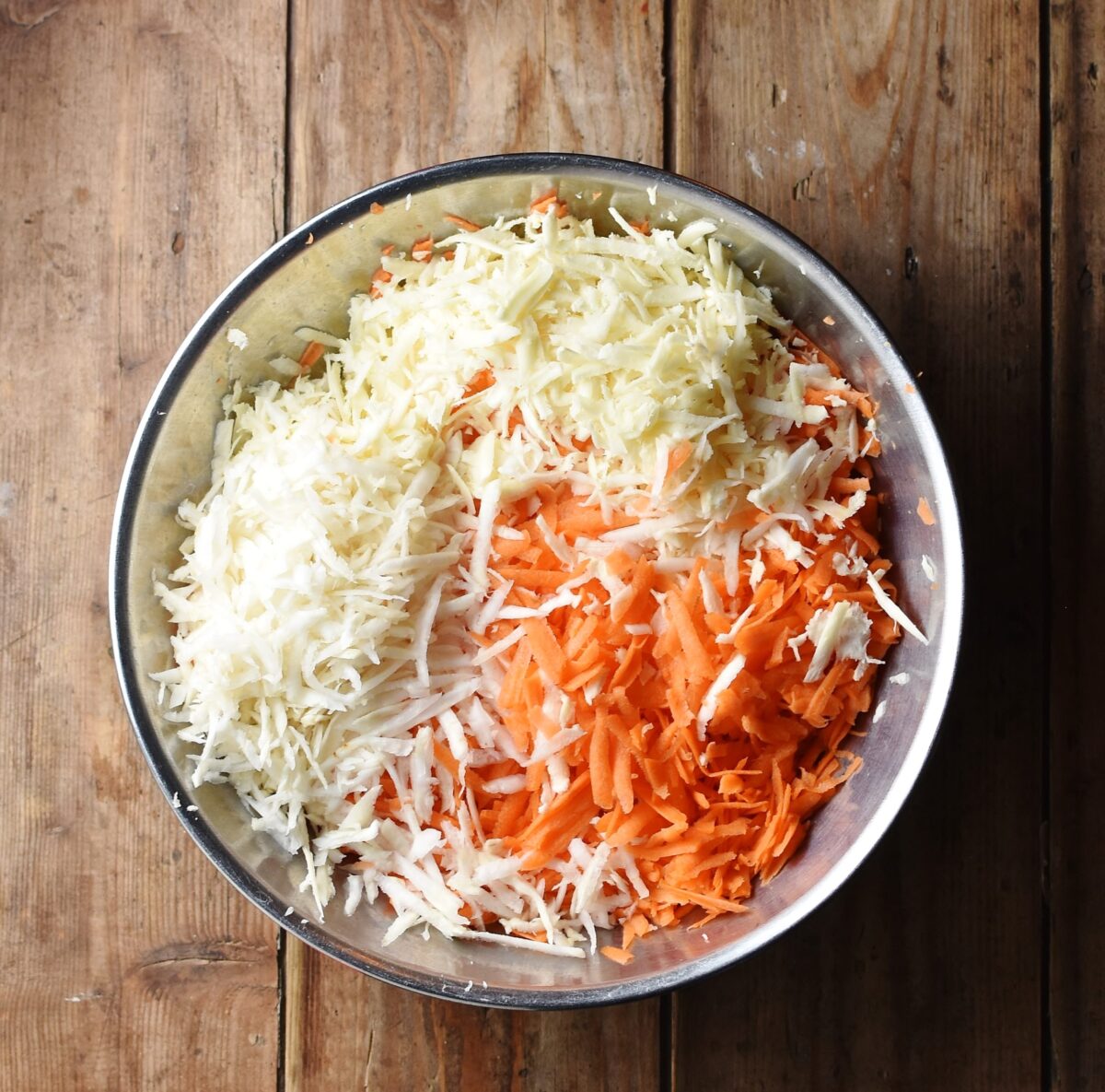 Grated carrot and parsinp in large metal bowl.