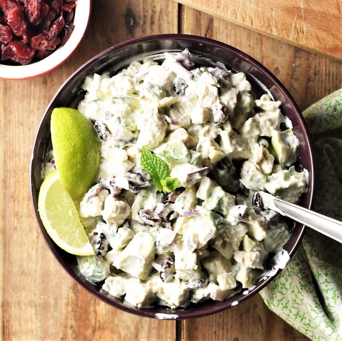 Turkey and cranberry creamy salad with lime wedges in purple bowl with spoon.