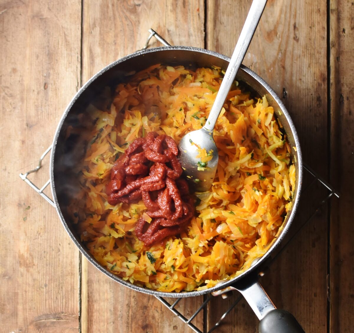 Stewed grated vegetables with tomato paste in large pot with spoon.