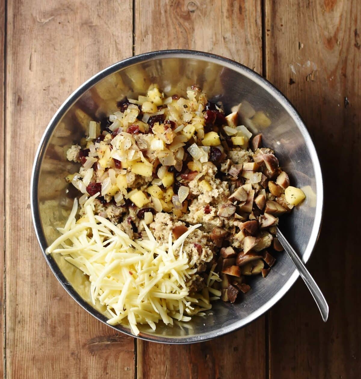 Chopped chestnuts, grated cheese and sausage mixture in large metal bowl with spoon.