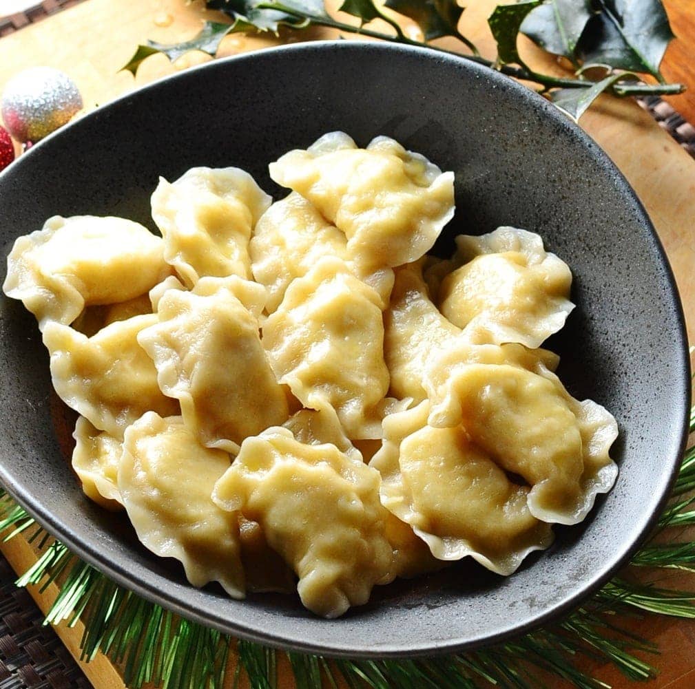 Close-up view of potato and cheese pierogi in black bowl with Christmas decorations on top of wooden table.
