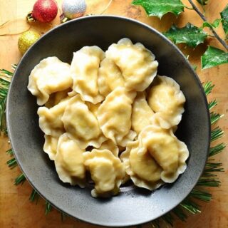 Top down view of Polish pierogi in black bowl on top of wooden table with Christmas decorations.