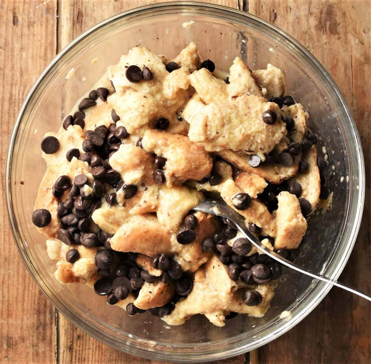 Bread in egg mixture with chocolate chips in mixing bowl.