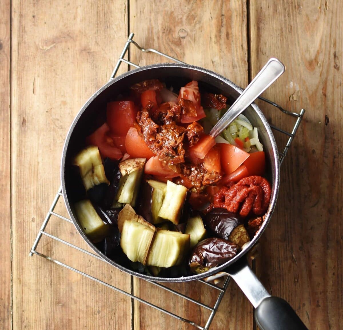 Chopped tomatoes and eggplant in large pot with spoon.