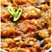 Eggplant in tomato sauce in white oval dish with chopped green chillies.
