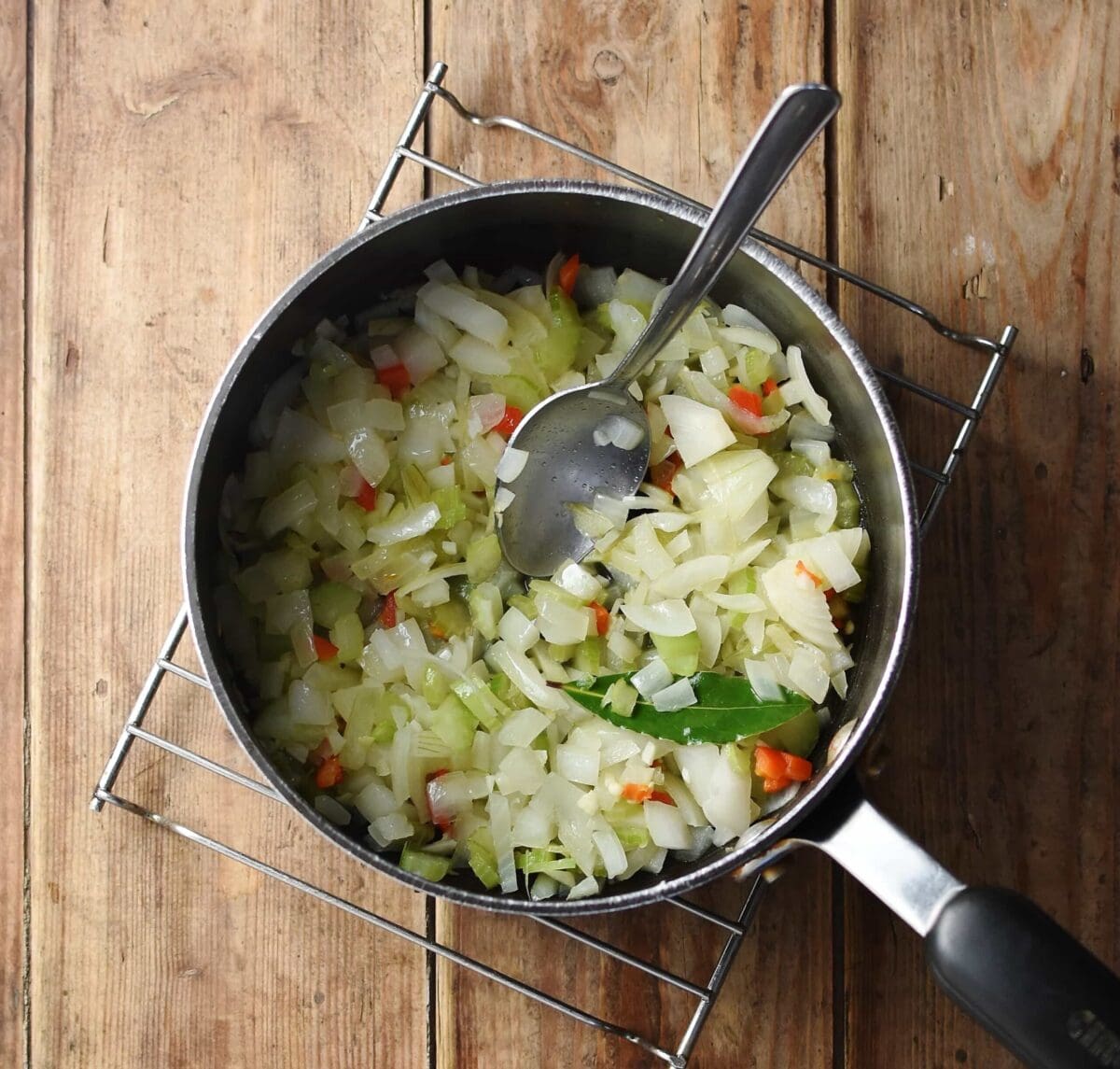 Chopped onion, chilli and bay leaf in large pot with spoon.