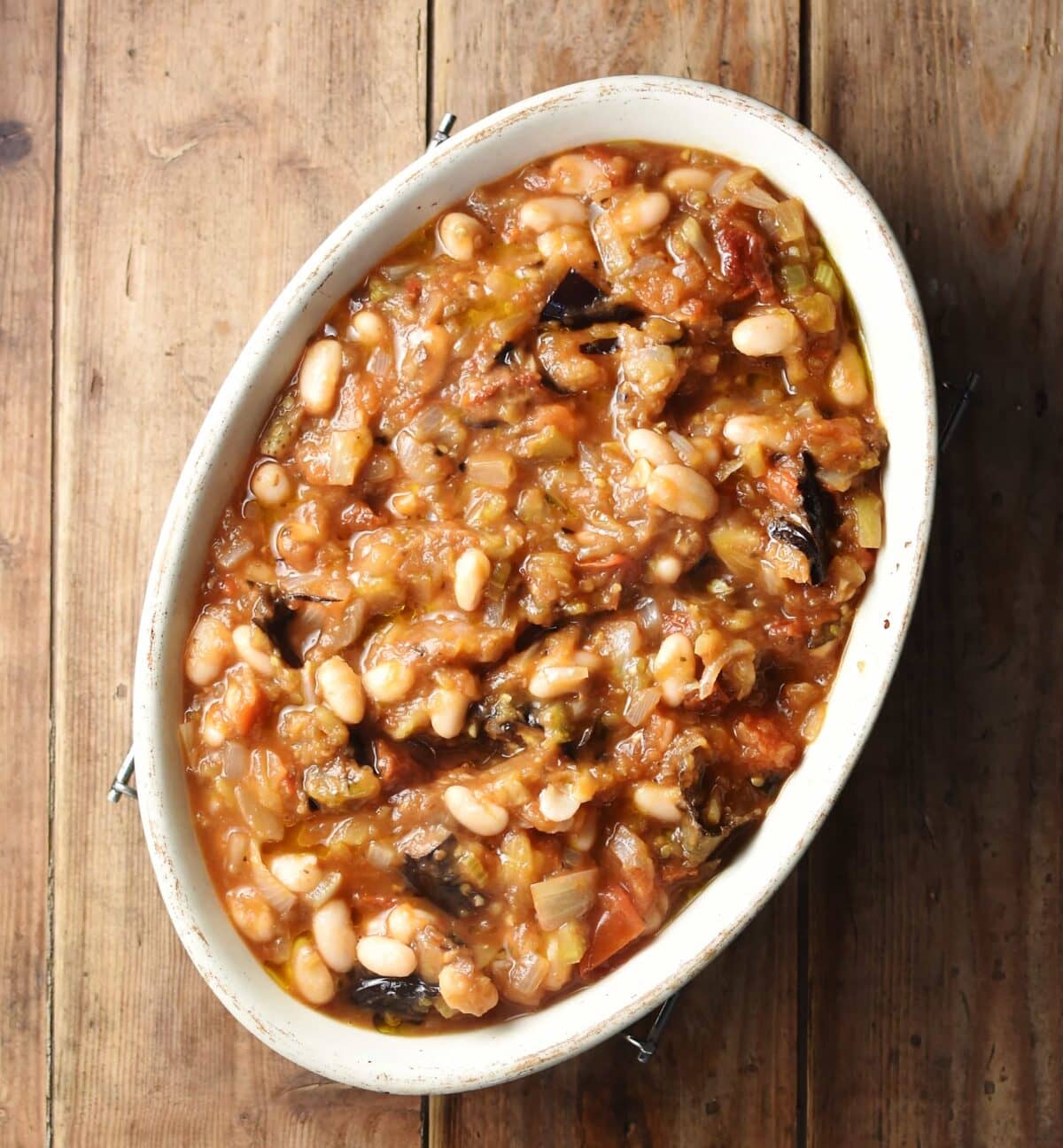 Eggplant and beans in thick tomato sauce inside white oval casserole dish.