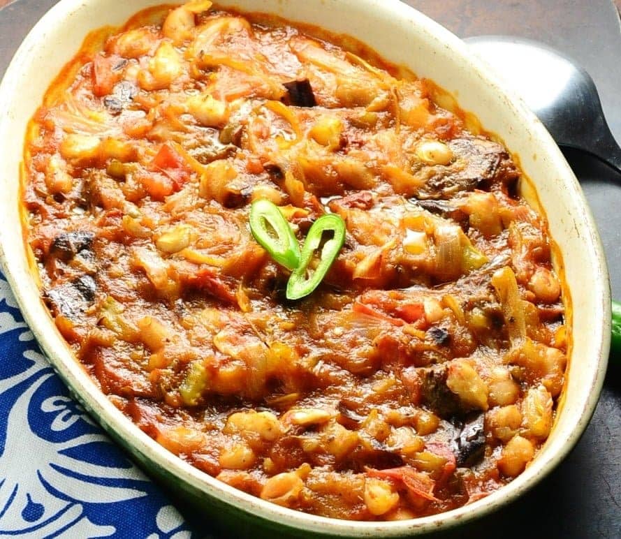 Eggplant tomato casserole in white oval dish with spoon and blue-and-white cloth.