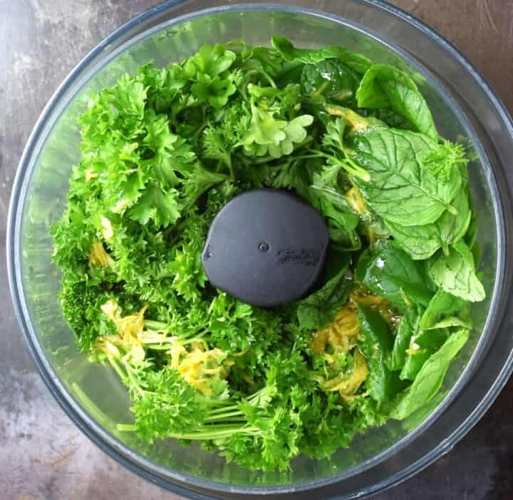 Fresh parsley stalks and mint leaves in food processor bowl. 