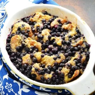 Blueberry french toast in white oval dish and blue-and-white cloth to left.