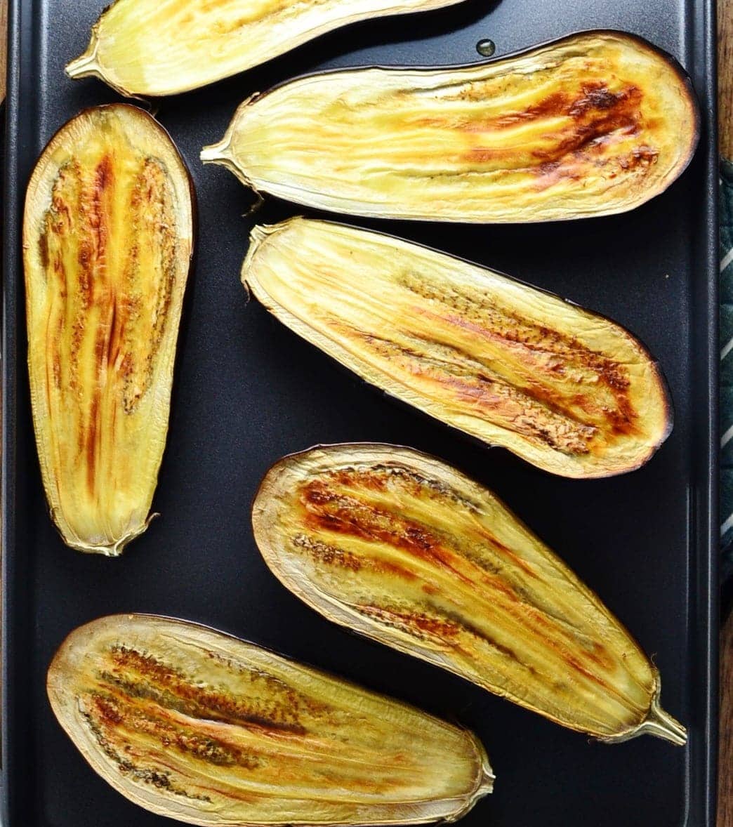 Roasted eggplant halves on oven tray.