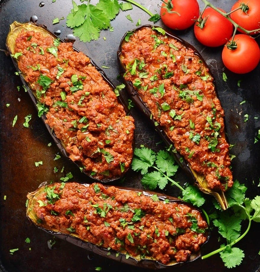 Top down view of baked stuffed eggplant with herbs and tomatoes on the vine on oven tray.
