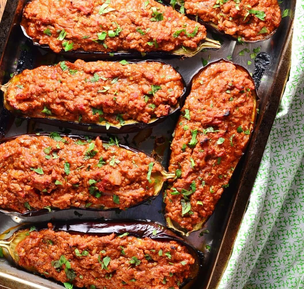 Top down view of stuffed eggplant on oven tray with green cloth to right.
