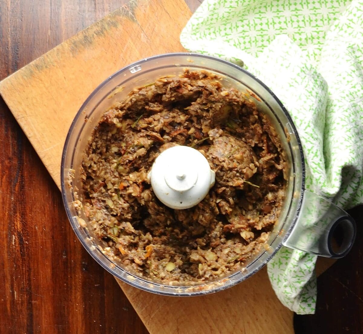 Mushroom mixture in blender bowl on wooden board with green cloth.