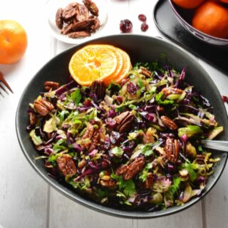 Top down view of Christmas slaw in black bowl with pecans and clementine in background.