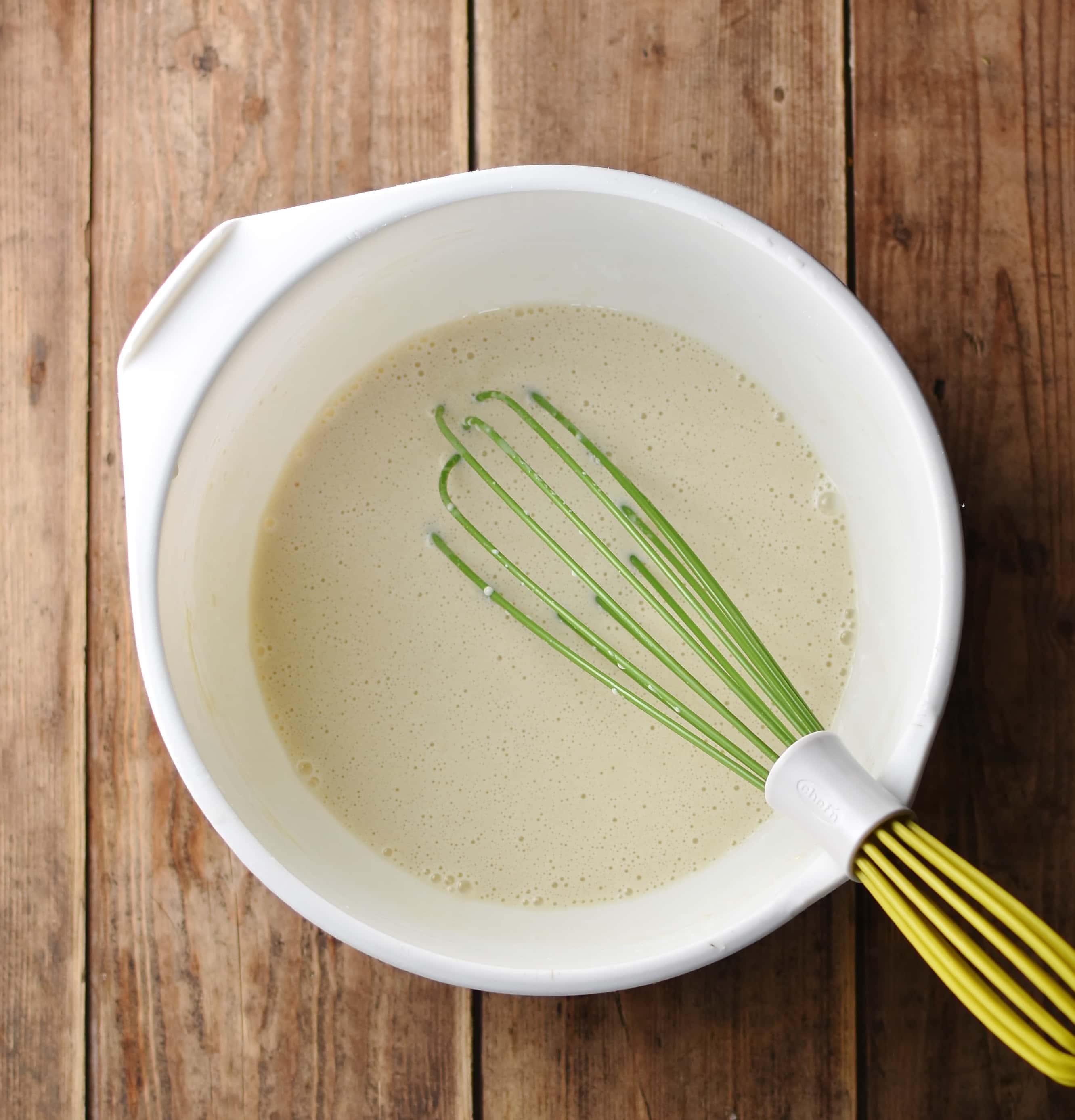 Crepes bstter in large white bowl with green whisk.