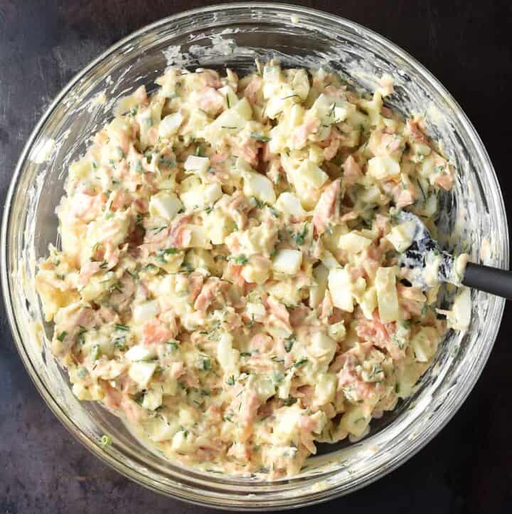 Assembled creamy salmon and egg salad in glass bowl with spoon. 