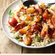 Close-up view of roasted fruit on top of quinoa with spoon on large white plate with green dish in background.