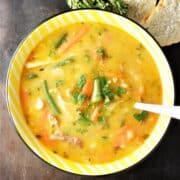 Top down view of leftover turkey soup with vegetables in yellow bowl.